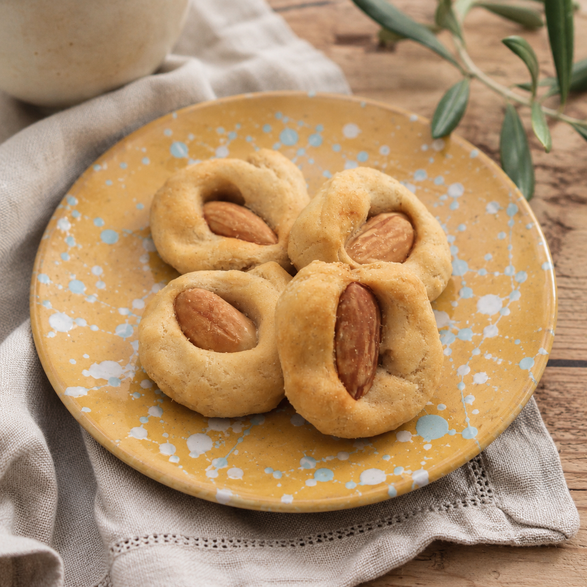 Taralli pugliesi con mandorle intere su piatto color ocra con schizzi di colore azzurro su tovagliolo di lino grigio su tavola di legno grezzo