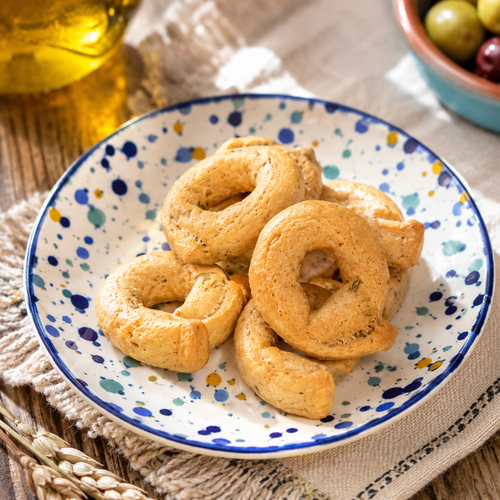 Taralli su piattino di ceramica bianco con pois colorati, su tovaglietta di cotone grigio su tavolo di legno grezzo