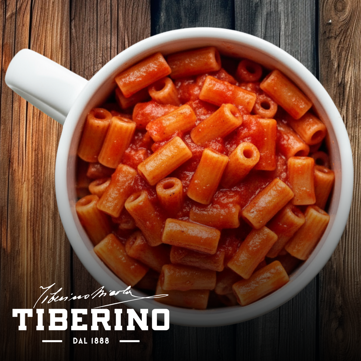 Pasta rigatoni con sugo rosso di pomodoro e basilico in una tazza bianca su sfondo di legno.