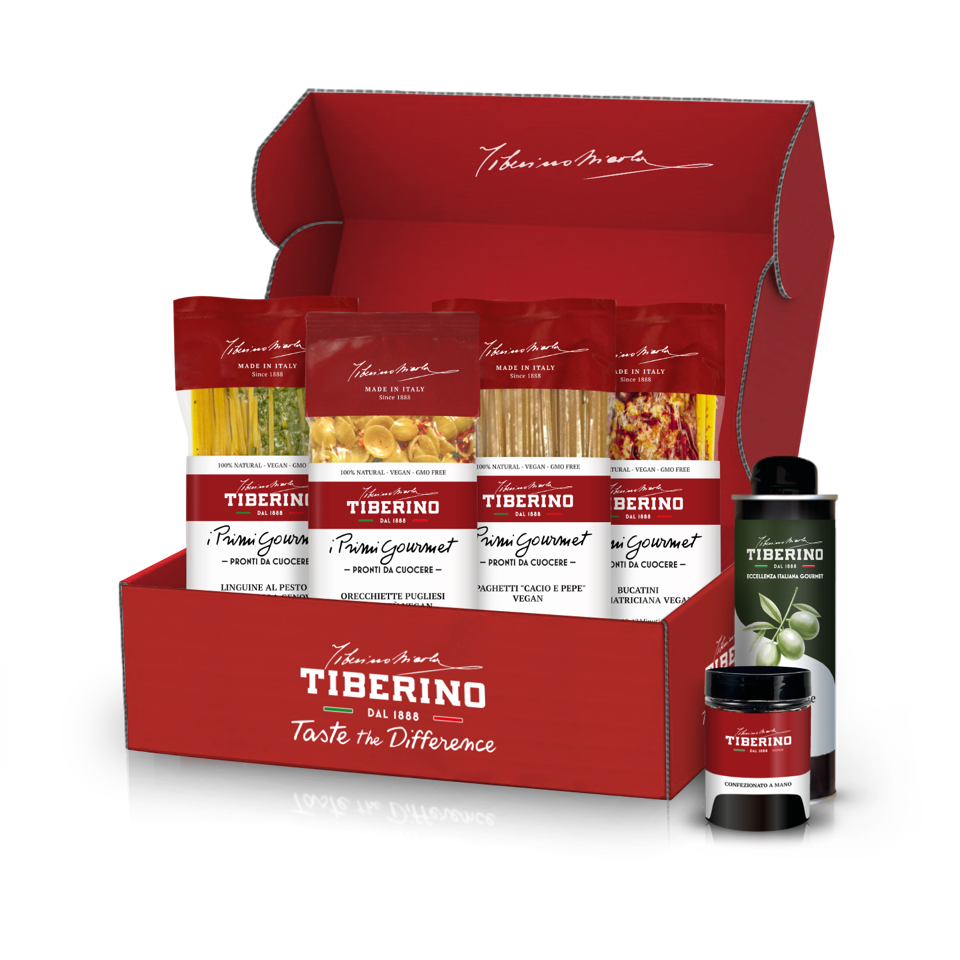 Scatola regalo rossa aperta di Tiberino 1888 con quattro confezioni di pasta vegana, una bottiglia di olio d'oliva e un vasetto.